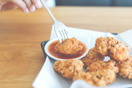 Hand of woman using a fork for take a fried chicken dipping to chilli sauce.の写真素材