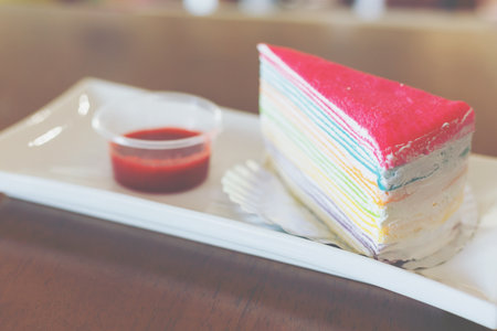 Rainbow crepe cake with a strawberry jam on white dish.