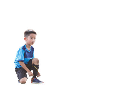Young Asian football player in blue jersey tied his shoelace between competition, isolated on white background.の写真素材