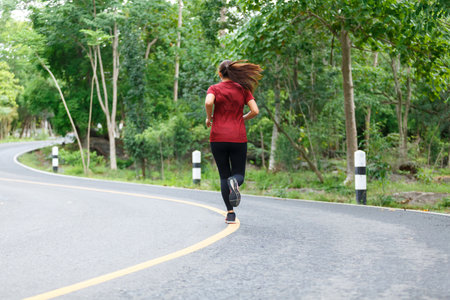 Back of woman runner and runing at the road surround with green forest.の写真素材