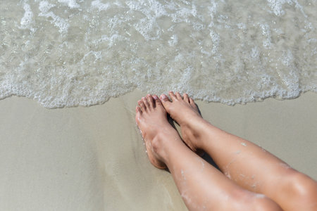Woman feet on white sand beach with sea wave.の写真素材