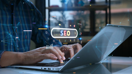 Person uses a laptop with various digital SEO icons and graphs overlaid, symbolizing online marketing and search engine optimization.の写真素材