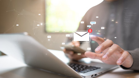 A person using a smartphone and laptop to check new email notifications, symbolizing digital communication and online connectivity.の写真素材