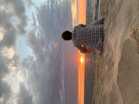 Young man sitting on the beach and looking at the sunset sky.の写真素材