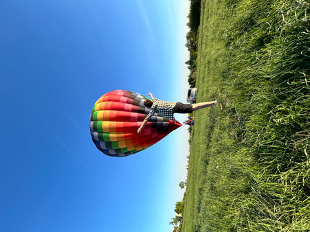 Colorful hot air balloon flying in the blue sky over green field.の写真素材