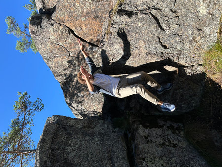Young man climbing on a rocky wall with blue sky in the background. Karelia, Ladoga, Lake Ladoga, Ladoga skerriesの写真素材