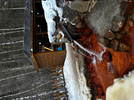 Abandoned wooden house in winter forest with frozen waterfall and iciclesの写真素材