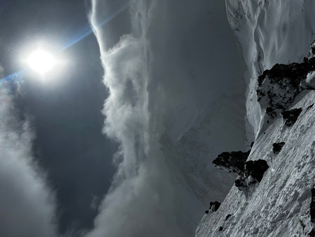 Snowy mountain peak in the clouds with sun and sun beams.の写真素材