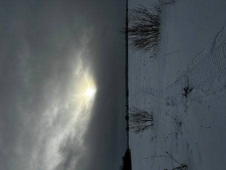 Snowy winter landscape with sun in the sky and dark clouds.の写真素材