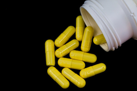 Yellow pill capsules with white pill container on black background