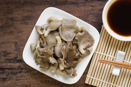 close up of steamed phoenix mushroom in a ceramic plate served with soy sauce on old wooden table....