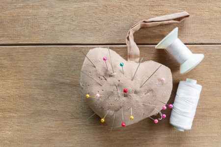 top view of old handmade sewing cushion with needle pin and thread on wooden table. craft and embroidery conceptの写真素材
