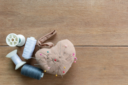 top view of old handmade sewing cushion with needle pin and thread on wooden table. craft and...