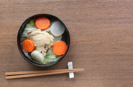 top view of chicken thigh clear soup with vegetable in a ceramic bowl on wooden table. asian homemade style food concept.の写真素材