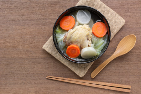 top view of chicken thigh clear soup with vegetable in a ceramic bowl on wooden table. asian homemade style food concept.の写真素材