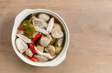 top view of spicy straw mushroom soup with chicken in a ceramic bowl on wooden table. asian homemade style food concept.の写真素材