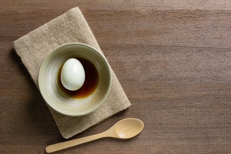 top view of boiled egg with soy sauce in a ceramic bowl on wooden table, copy space for text. cheap nutrition source concept.の写真素材