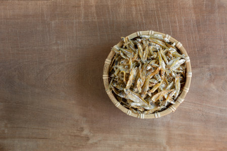 top view of raw dried little fish in a bamboo basket on wooden table. asian style food concept.の写真素材