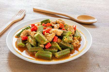 close up of stir fried okra with red curry paste and pork in a ceramic dish on wooden table. hot and spicy thai style food menu.の写真素材