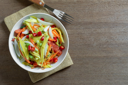top view of spicy mango salad in a ceramic bowl on wooden table. asian homemade style food concept.の写真素材
