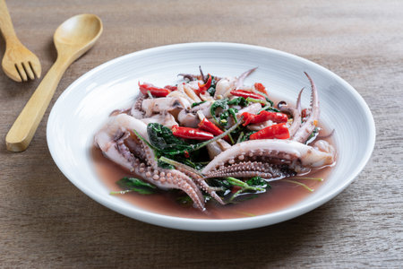 Stir fried squid tentacle with holy basil in a ceramic dish on wooden table.の写真素材