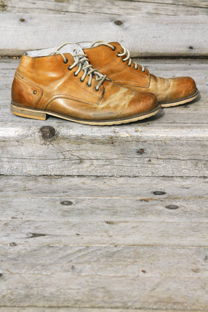 A pair of old leather boots on background wooden wall of a house 