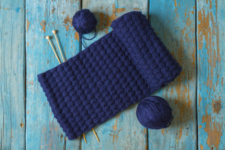 Two coils of wool and a knitted scarf with knitting needles on an old wooden table