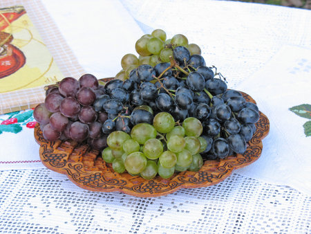 Grapes on a wooden plate with pattern and white canvasの写真素材