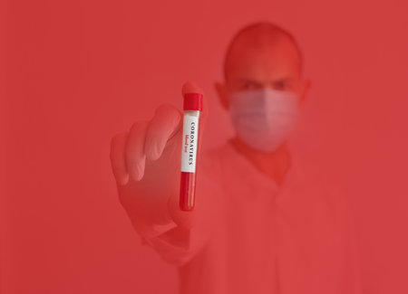 Doctor wearing a medical face mask and gloves, holding a blood test for the Coronavirus COVID-19 outbreak, red background.の写真素材