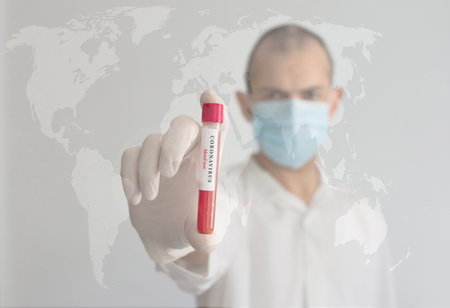 Coronavirus conceptual photo with doctor wearing a medical face mask and gloves, holding a blood test result for the COVID-19 pandemic and blurred world map in the backgroundの写真素材