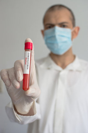 Doctor wearing a medical face mask and gloves, holding a blood test result for the Coronavirus COVID-19 outbreak. Coronavirus blood test conceptual photo.の写真素材