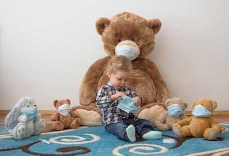Child playing with his sick teddy bears wearing medical mask against viruses. Role playing, child playing doctor with plush toy. Children and flu, coronavirus illness concept. Selective focusの写真素材