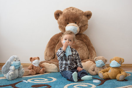 Child playing with his sick teddy bears wearing medical mask against viruses. Role playing, child playing doctor with plush toy. Children and flu, coronavirus illness concept. Selective focusの写真素材