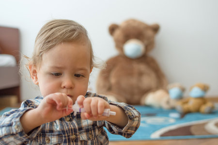 Child playing with his sick teddy bears wearing medical mask against viruses. Role playing, child playing doctor with plush toy. Children and flu, coronavirus illness concept. Selective focusの写真素材