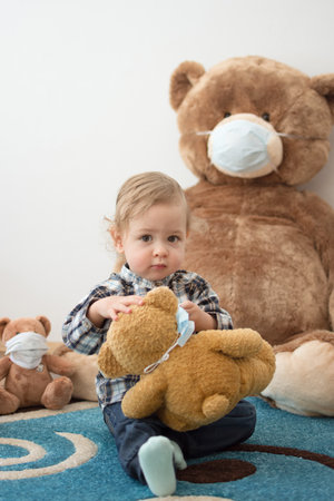 Child playing with his sick teddy bears wearing medical mask against viruses. Role playing, child...