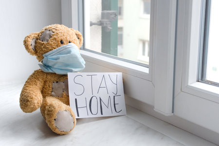 Sick teddy bear in home quarantine wearing a medical mask against viruses during coronavirus and flu outbreak, with the advice to stay home.の写真素材