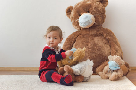 Child playing with his sick teddy bears wearing medical mask against viruses. Role playing, child playing doctor with plush toy. Children and illness concept.の写真素材