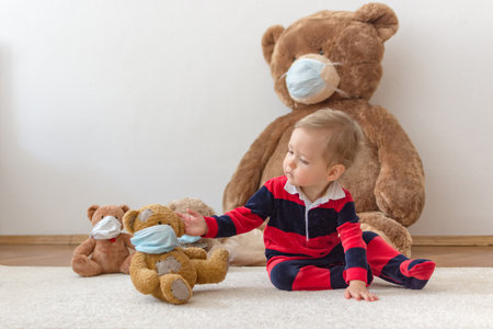 Child playing with his sick teddy bears wearing medical mask against viruses. Role playing, child playing doctor with plush toy. Children and illness concept.の写真素材