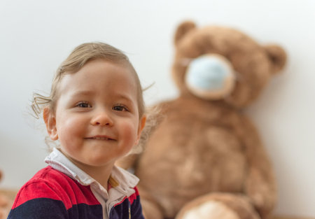 Child playing with his sick teddy bears wearing medical mask against viruses. Role playing, child playing doctor with plush toy. Children and illness concept.の写真素材