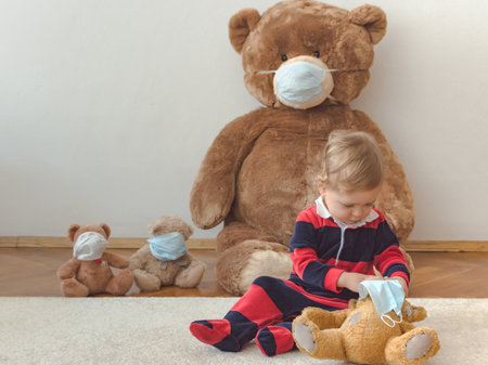 Child playing with his sick teddy bears wearing medical mask against viruses. Role playing, child playing doctor with plush toy. Children and illness concept.の写真素材