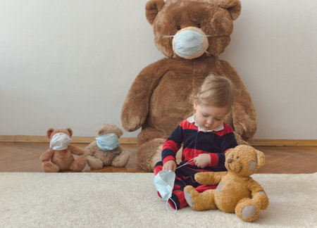 Child playing with his sick teddy bears wearing medical mask against viruses. Role playing, child playing doctor with plush toy. Children and illness concept.の写真素材