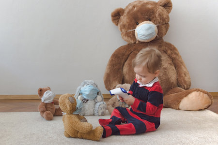 Child playing with his sick teddy bears wearing medical mask against viruses. Role playing, child playing doctor with plush toy. Children and illness concept.の写真素材