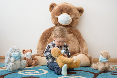Child playing with his sick teddy bears wearing medical mask against viruses. Role playing, child playing doctor with plush toy. Children and flu, coronavirus illness concept. Selective focusの写真素材