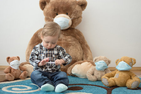Child playing with his sick teddy bears wearing medical mask against viruses. Role playing, child playing doctor with plush toy. Children and flu, coronavirus illness concept. Selective focusの写真素材