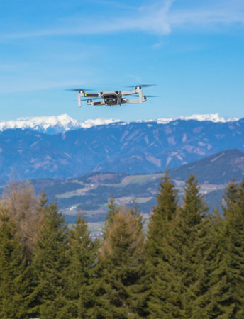 White drone with photo camera flying in the blue sky and beautiful mountain landscape in the backgroundの写真素材