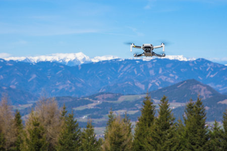 White drone with photo camera flying in the blue sky and beautiful mountain landscape in the backgroundの写真素材