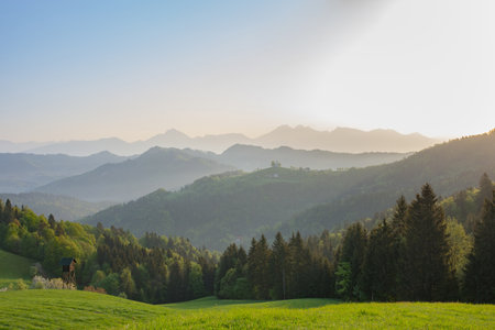 Slovenian breathtaking landscape at sunrise with Julian Alps and charming little church of Sveti Tomaz (Saint Thomas) on a hill, in spring. Beautiful misty morning in the mountains, in Slovenia.の写真素材