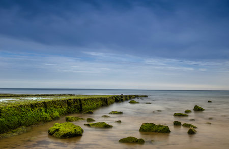 Flanked by tall cliffs, the lovely Porto de MÃ³s Beach is like a long tongue of golden sand. At low tide the rocks at the end of the beach are exposed. In Lagos,Western Algarve coastline, Portugal.の写真素材