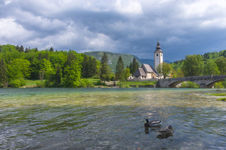 The charming little Church of St. John the Baptist on lake Bohinj, Julian Alps, the largest permanent lake in Slovenia. Beautiful spring colors and dramatic skyの写真素材