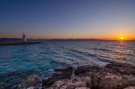 Wild coast of the Aegina island and the old small lighthouse in the background, Saronic gulf, Greece, at sunset.の写真素材